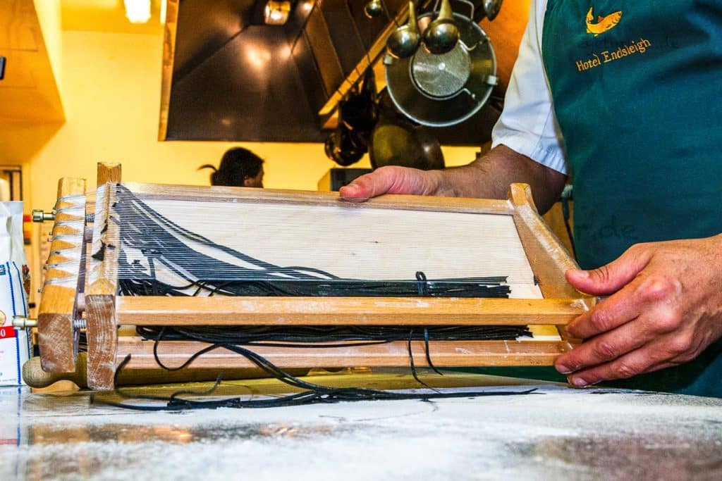 Die einzelnen Schritte der Pastaproduktion mit dem Carraturo. Zuerst wird der Teig mehrmals durch eine Nudelmaschine gedreht, bis er ganz dünn ist. Danach kann der dünne Teiglappen mit einem Nudelholz durch die Drähte gedrückt werden, die ihn in dünne Streifen schneiden. Anschließend kurz bemehlen und erst kurz vor dem Verzehr in Salzwasser al dente kochen. An der Seite des Chefkochs steht Salvatore Piacente, ebenfalls Absolvent der Kochschule Santa Maria, an der schon José Graziosi sein Handwerk lernte / © Foto: Georg Berg