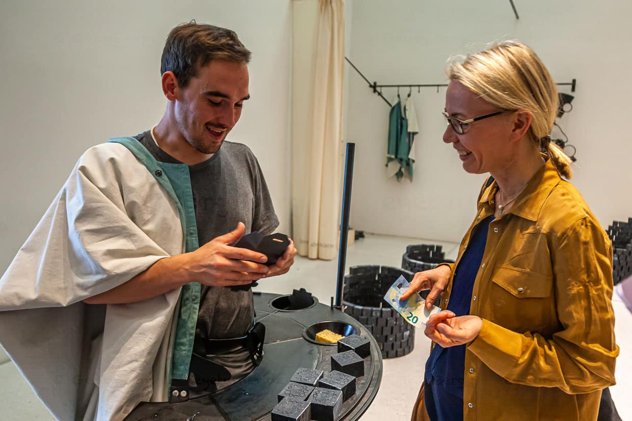 Mitten im Verkaufsgespräch: Angela Berg fragt Kunststudenten Viktor nach den 7 Ölen der Seife von Künstlerin Otobong Nkanga / © Foto: Georg Berg