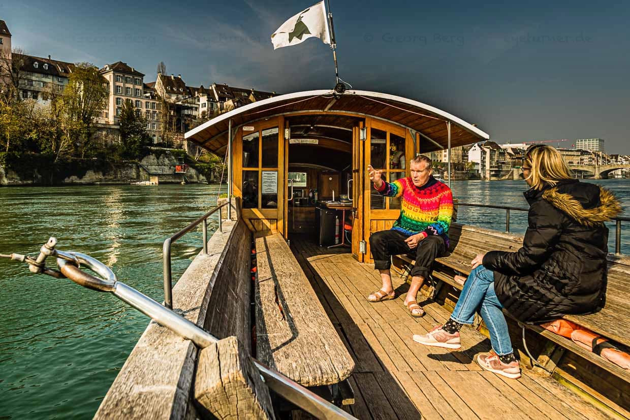 Jacques Thurneysen, in Paris geboren und auf dem Rhein zuhause: Seit vielen Jahrzehnten hält er die Pacht für die kleine Seilfähre, die über den Schwengel mit einem Drahtseil verbunden ist, das das Basler Münster mit dem anderen Ufer verbindet. Mit 65 Jahren übergibt Thurneysen die Pacht an seinen Sohn Noa. Im Sommer ist die Fähre 77 Stunden in der Woche im Dienst. Die Schichten teilt sich Jacques Thurneysen mit Sohn und Neffe / © Foto: Georg Berg