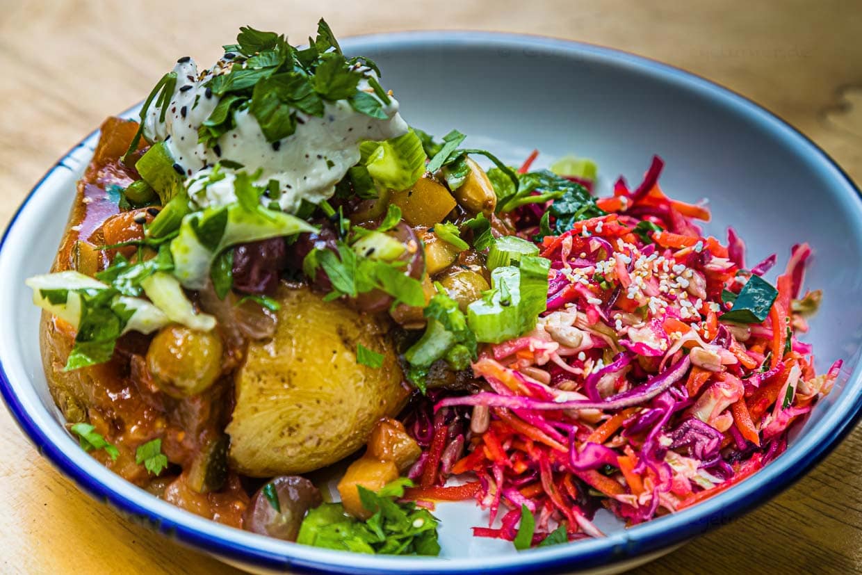 Caponata, wahlweise vegetarisch oder vegan. Mit Aubergine, Zucchini, Cocktailtomate, Zwiebel, Mandeln, Staudensellerie, Traube. Wahlweise mit Labneh, einem orientalischen Frischkäse mit Kräutern. Im Zentrum eine gebackene Bio-Kartoffeln der Sorte Agria, gewachsen in Olching vor der Toren Münchens / © Foto: Georg Berg