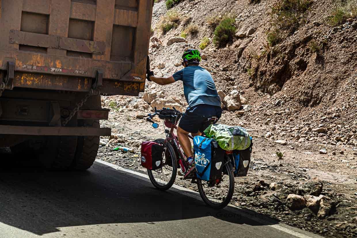Ein Fahrradtourist lässt sich in Tadschikistan von einem LKW den Takfon-Pass hochziehen. Im Schlepptau von Transportern  lassen sich gerne mehrere Hundert Höhenmeter überwinden / © Foto: Georg Berg