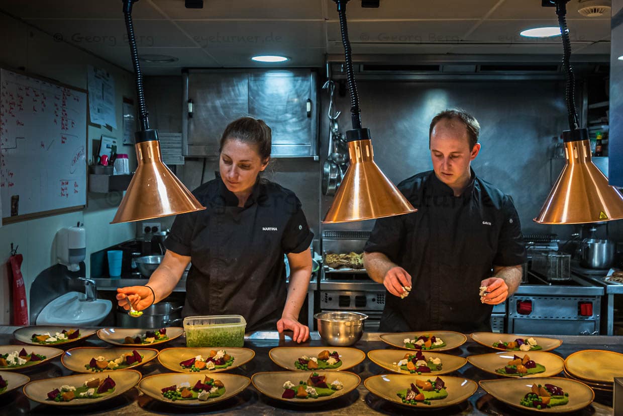 Mit Standfestigkeit und ruhiger Hand: Martina und Gavin richten in der Kombüse trotz Seegang das Hauptgericht an / © Foto: Georg Berg