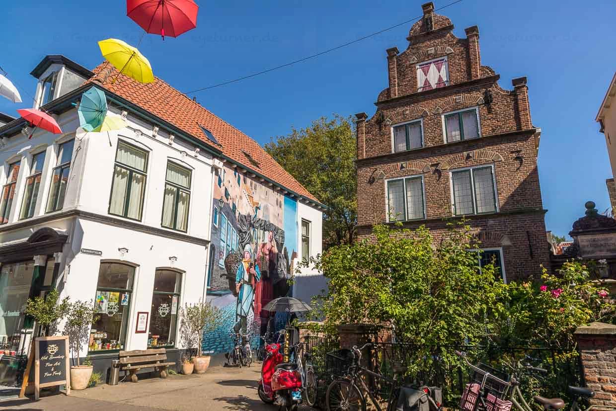 Wandmalerei in der Altstadt von Deventer. Motiv anlässlich des Hansejahres, das die neun holändischen Hansestädte 2023 feiern. Die Wandmalerei hat einen Bezug zur Vergangenheit und Gegenwart. Hier in Deventer: Marktfrau mit Sohn verkauft Deventer Honigkuchen und Stockfisch, wichtige Waren im Hansehandel von Deventer. Der Junge trägt einen Fan-Schal des Fußball-Clubs Deventer Eagles / © Foto: Georg Berg