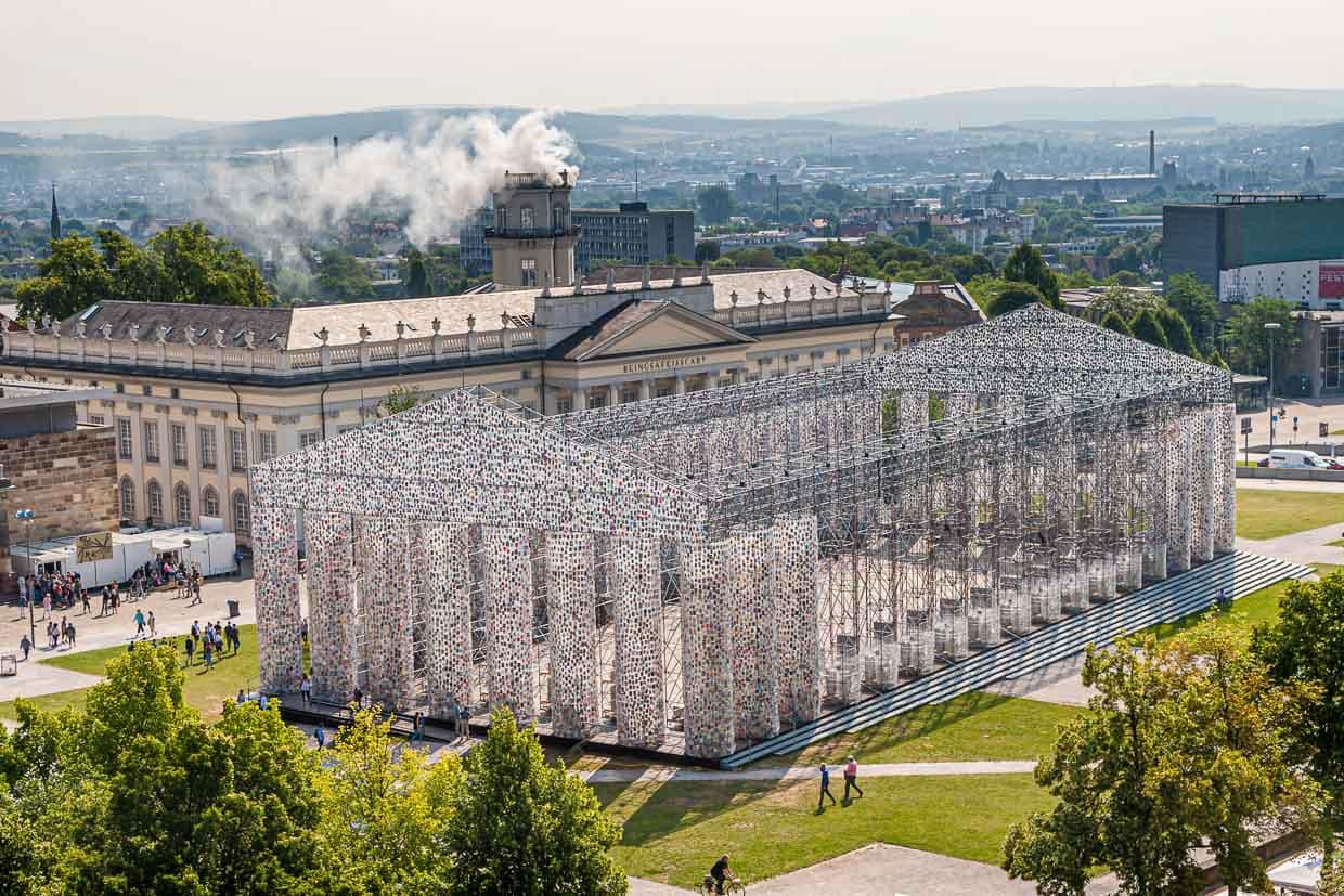 Parthénon des livres, de l'artiste argentine Marta Minujin à la documenta 14 de Kassel. Chaque jour, la construction, dont les dimensions sont une réplique du temple de l'Acropole, devenait plus massive et s'enrichissait de nouveaux livres. En arrière-plan, l'installation "Expiration Movement" fume dans la Zwehrenturm. / © Photo : Georg Berg