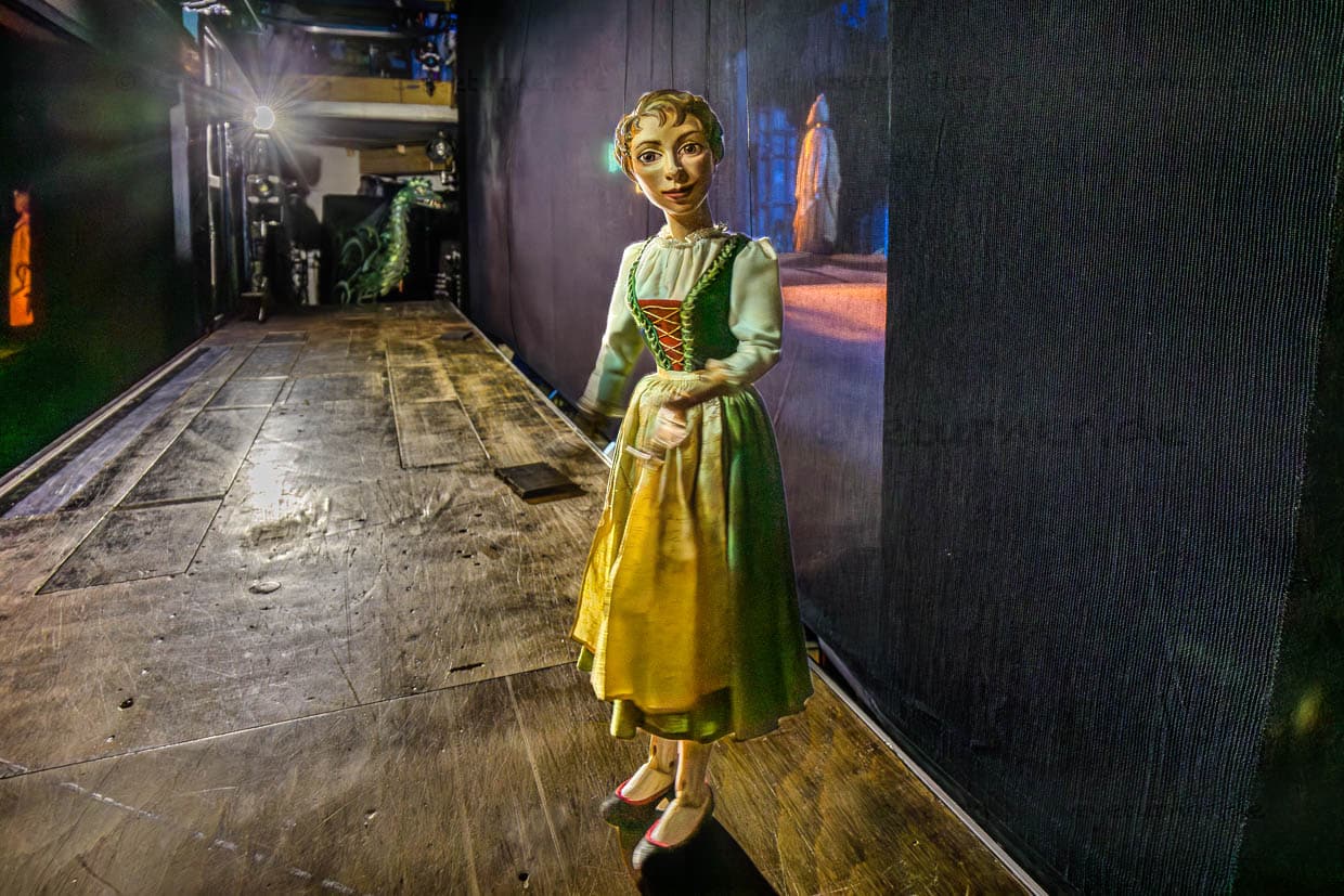 Eine beleuchtete Marionette im Dirndl steht vor einer Projektionswand auf einer Bühne in der Bristol-Passage, Salzburg, Austria