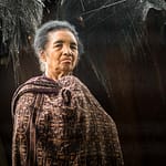 Frau in traditioneller Kleidung vor einer Hütte / © Foto: Georg Berg