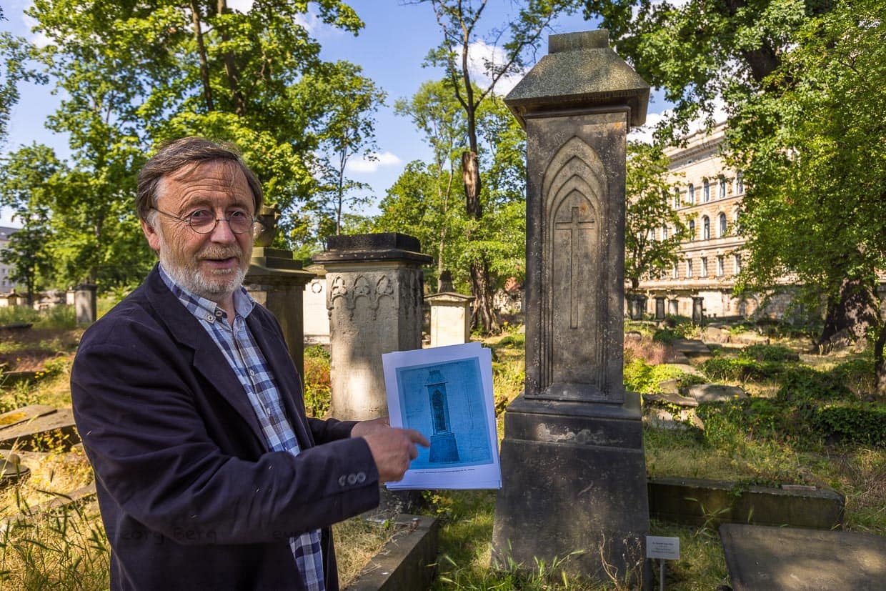 Volker Neumeister vom Förderverein Eliasfriedhof an einer Grabsäule nach dem Entwurf von Caspar David Friedrich. Hier das Grab von Dr Christian Ernst Ulrici, gstorben 1825. Volker Neumeister hält den Entwurf des Malers für ein Pfeilergrabmal mit Kreuz in gotischen Spitzbögen in der Hand / © Foto: Georg Berg