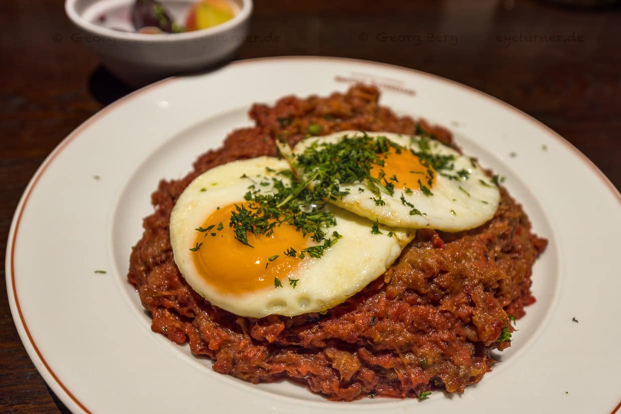 Sablé traditionnel de marin composé de poitrine de bœuf salée et de pommes de terre en purée avec du rollmops, deux œufs au plat, betteraves rouges et cornichons à la moutarde / © Foto : Georg Berg