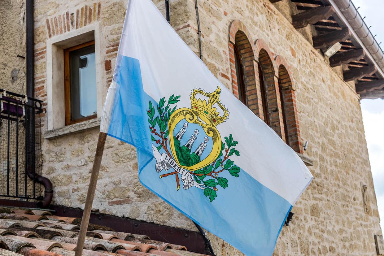 Le drapeau aux armoiries de Saint-Marin est un symbole de liberté et d'indépendance. Il se compose d'un écu bleu avec trois montagnes vertes, trois tours d'argent, une sur chaque montagne, chaque tour étant ornée d'une plume d'argent. La devise Libertas, qui signifie liberté en latin, ainsi qu'une couronne, symbole de la souveraineté exercée / © Photo : Georg Berg