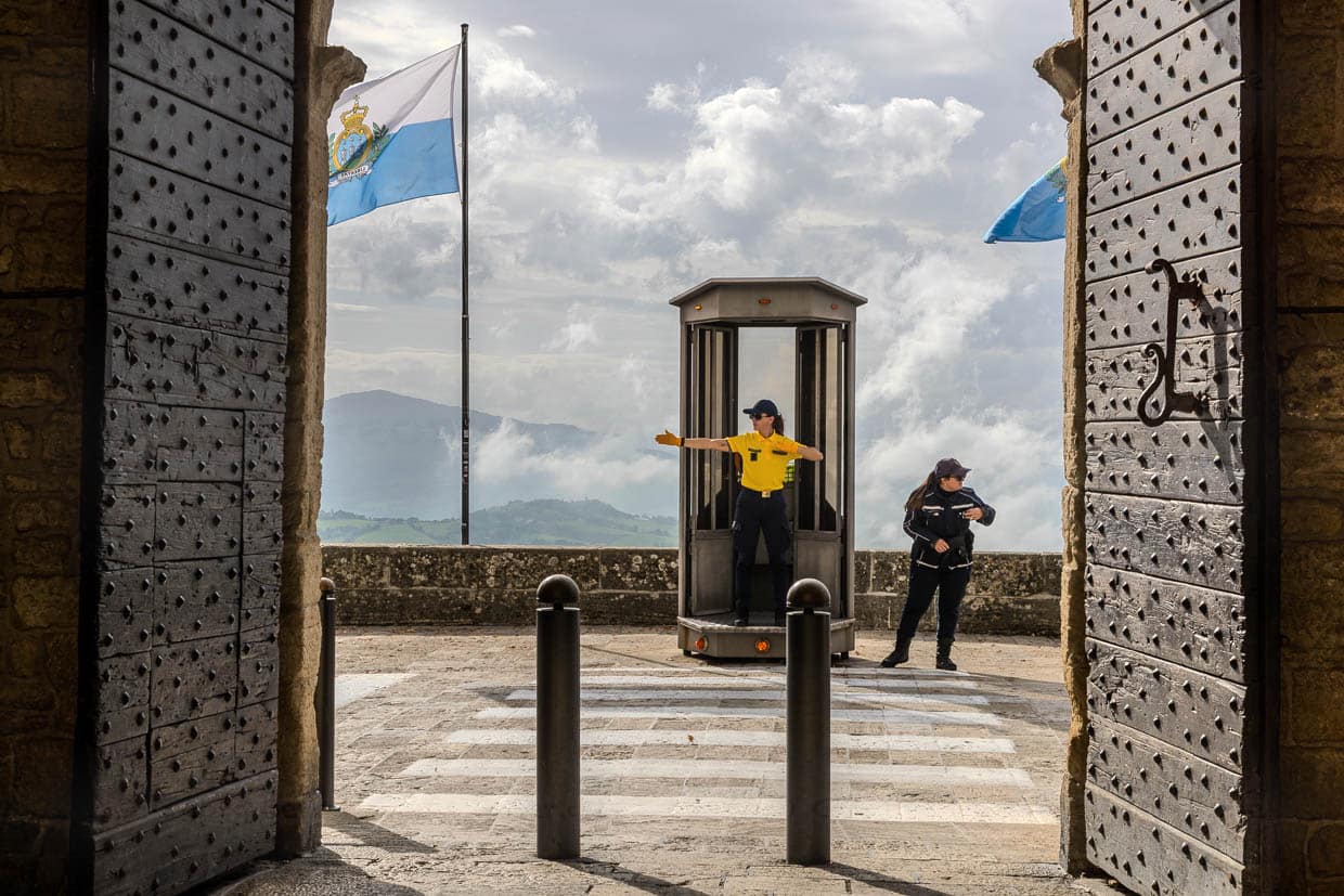 Une policière régule le trafic routier sur la route d'accès au centre historique de Saint-Marin. Ici, vue à travers la porte des remparts sur le passage piéton et la policière de la circulation / © Foto : Georg Berg