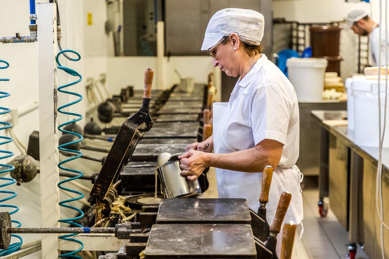 Une employée verse de la pâte à gaufres dans le lourd gaufrier. Au bout de quatre minutes, la gaufre est cuite. La Torta Tre Monti est composée de plusieurs couches de gaufres et de chocolat noir / © Foto : Georg Berg