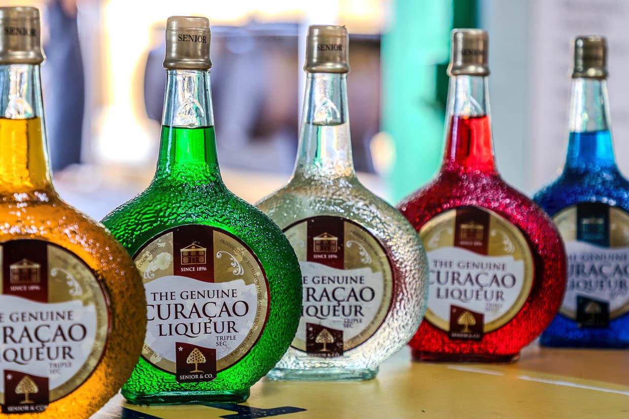 La liqueur de curaçao authentique produite à Curaçao par Senior à la Landhuis Chobolobo Distillery est un distillat initialement incolore d'écorces d'orange Lahara macérées. Les colorants alimentaires ajoutés peuvent la colorer en rouge, jaune, vert ou (le plus connu) en bleu / © Photo : Georg Berg