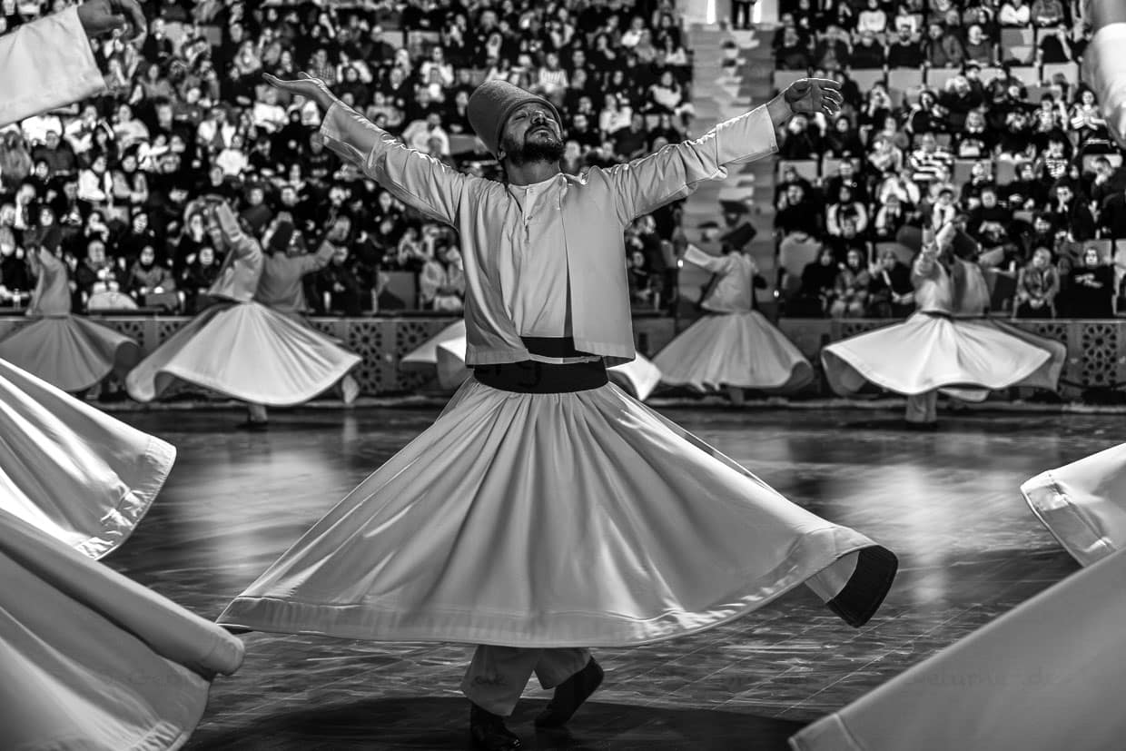 Şeb-i Arus-Zeremonie im 3.000 Personen fassenden Mevlana Kültür Merkezi. Beim Sufi-Wirbeltanz zeigt die rechte Hand nach oben und empfängt Gottes Segen. Die linke Hand zeigt nach unten und gibt den Segen an die Erde weiter. Sie drehen sich gegen den Uhrzeigersinn (symbolisch gegen das Ego). Der rechte Fuß bleibt fest, der linke treibt die Drehung an / © Foto: Georg Berg