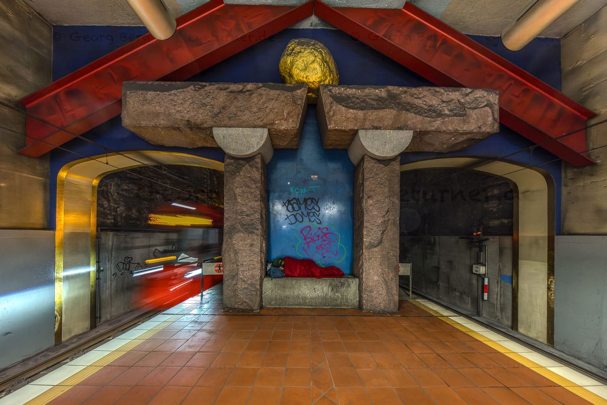 Eine obdachlose Person schläft auf einer Steinbank in der U-Bahn-Station Venloer Straße, Cologne, Germany während eine Bahn vorbeifährt