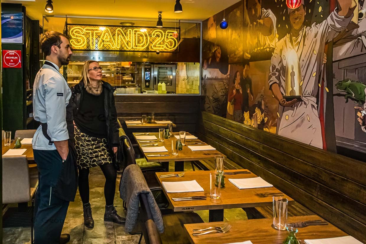 Angela Berg mit Koch László Papdi im Stand 25 vor der großen Cartoonzeichnung, die an den Bocuse d’Or Erfolg von Chefkoch Támás Szell erinnert. Dank des smarten Designs passen erstaunlich viele Gäste an den „Stand 25“ / © Foto: Georg Berg