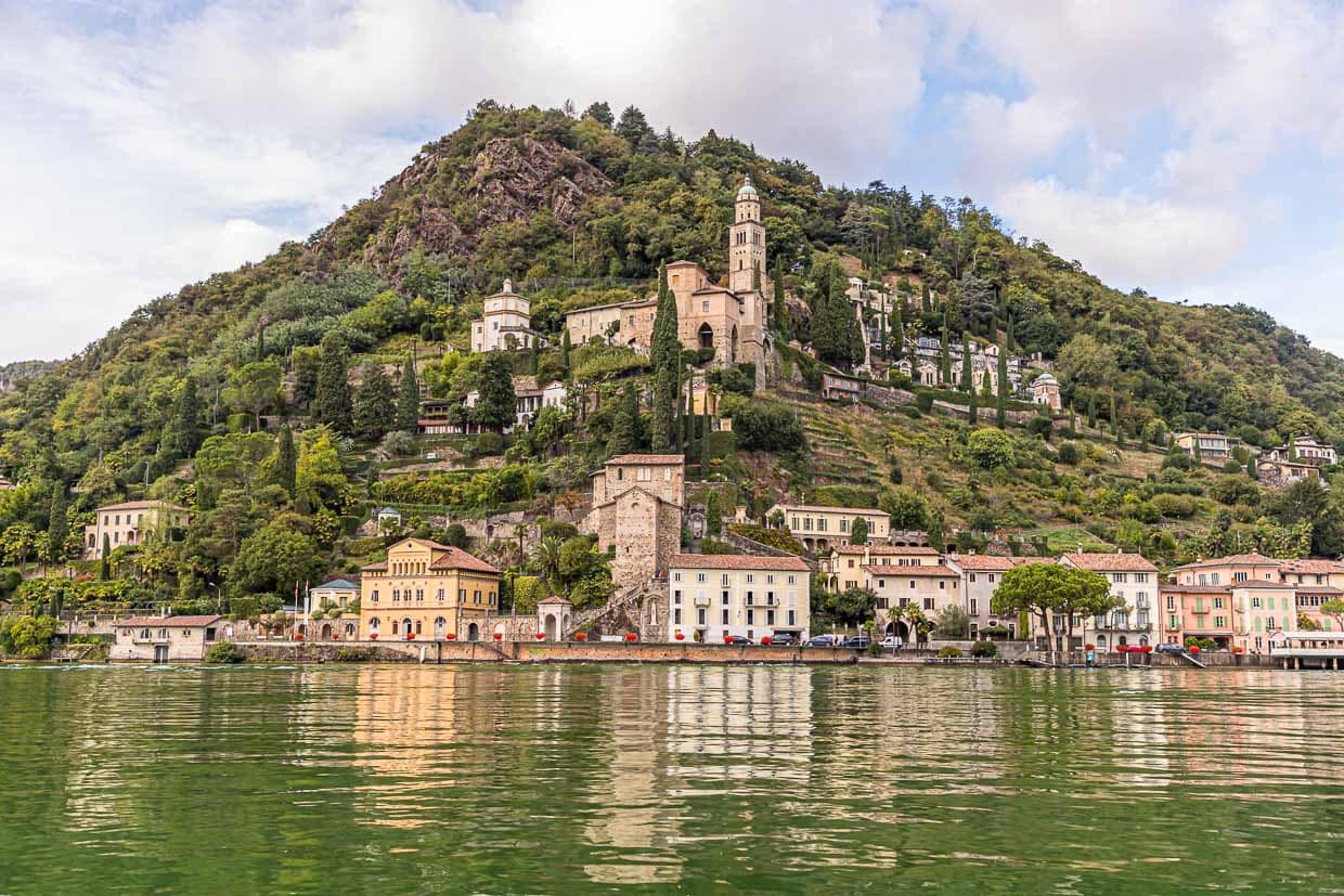 Vom Wasser aus betrachtet: Die Kirche Santa Maria del Sasso von Morcote, darunter die historische Altstadt. Viele kleine Restaurants säumen die Uferpromenade