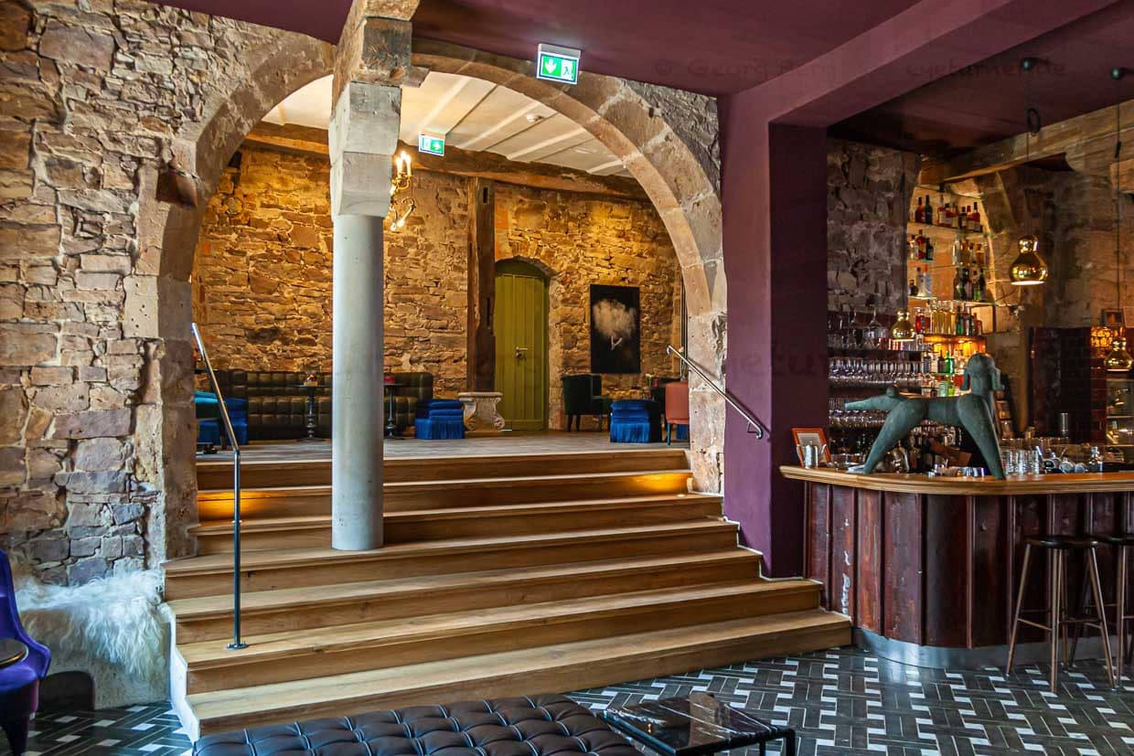 Pudelbar im Hotel Renthof, Kassel, Deutschland. Jeder Bogen ist ein Geschenk, sagt Mitinhaberin Kirstin Kleinkauf. Dieser Bogen, der den Eingangsbereich mit Bistro und Bar verbindet, ist ein besonderer Blickfang, an dem kein Gast achtlos vorbeigeht. Eine kleine Beobachtung am Rande: Beim Betreten der Bar interessieren sich die Männer mehr für die Statik des alten Steins, während die Frauen ihren Blick über die samtigen Sessel und funkelnden Lampen schweifen lassen / © Foto: Georg Berg