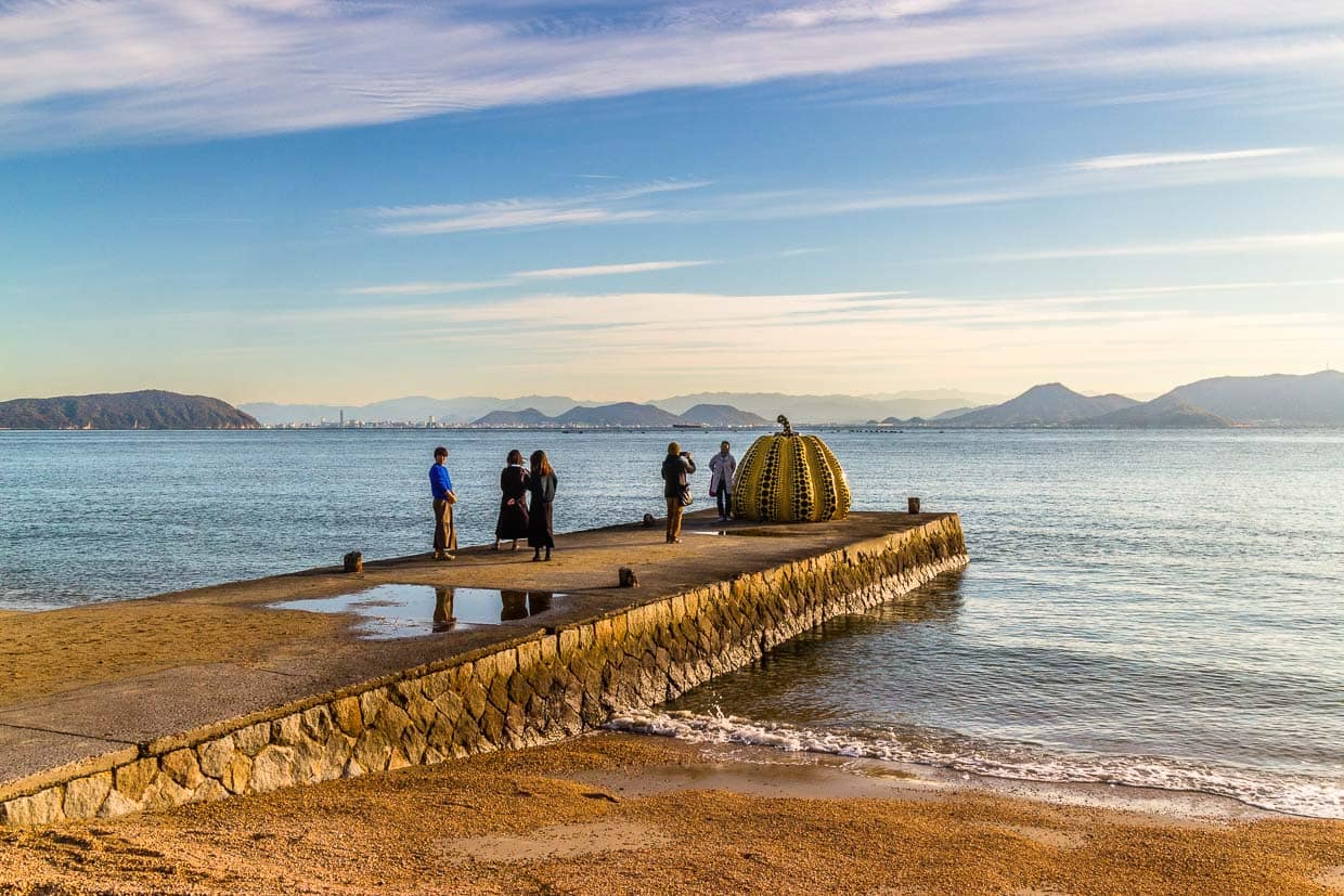 Steg mit Yellow Pumpkin von Yayoi Kusama. Der berühmtem gelbe Kürbis wurde 2021 von einem Taifun isn Meer gespült. 2022 wurde an selber stelle ein neues Exemplar aufgestellt / © Foto: Georg Berg