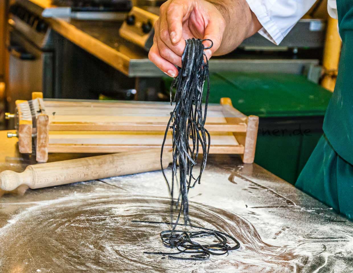 Die einzelnen Schritte der Pastaproduktion mit dem Carraturo. Zuerst wird der Teig mehrmals durch eine Nudelmaschine gedreht, bis er ganz dünn ist. Danach kann der dünne Teiglappen mit einem Nudelholz durch die Drähte gedrückt werden, die ihn in dünne Streifen schneiden. Anschließend kurz bemehlen und erst kurz vor dem Verzehr in Salzwasser al dente kochen. An der Seite des Chefkochs steht Salvatore Piacente, ebenfalls Absolvent der Kochschule Santa Maria, an der schon José Graziosi sein Handwerk lernte / © Foto: Georg Berg