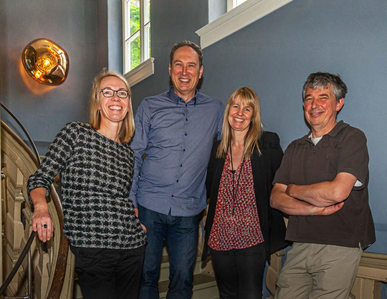 Treppenhaus mit Charakter. Es gibt zwar einen Fahrstuhl, aber wer auf diesen nicht angewiesen ist, sollte sich das Vergnügen machen und durch original knarzenden Barock mit schicken 1970er Leuchten zu wandeln. Zudem ein Ort, an dem man sich gerne fotografieren lässt.: v.r.n.l. die Eigentümer Rainer Holzhauer, Kirstin Homburg-Kleinkauf und Uwe Kleinkauf zusammen mit Angela Berg / © Foto: Georg Berg