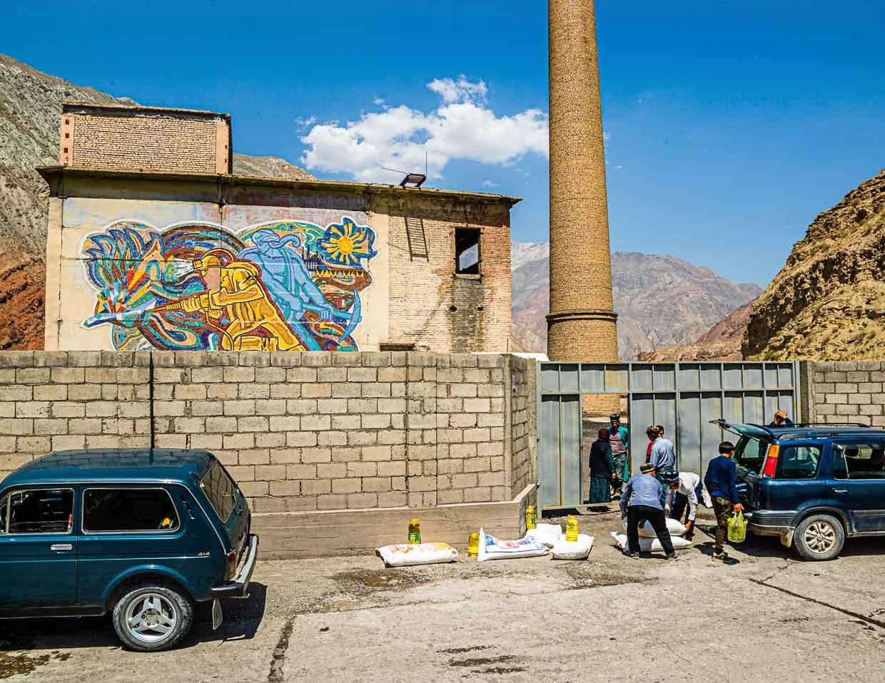 Hinter dem Fabriktor zieht ein Laster mit Grundnahrungsmitteln zahlreiche Interessenten an. Das Mosaik im Sowjetstil an der Fabrikmauer erinnert an den Bergbau in dieser Gegend / © Foto: Georg Berg