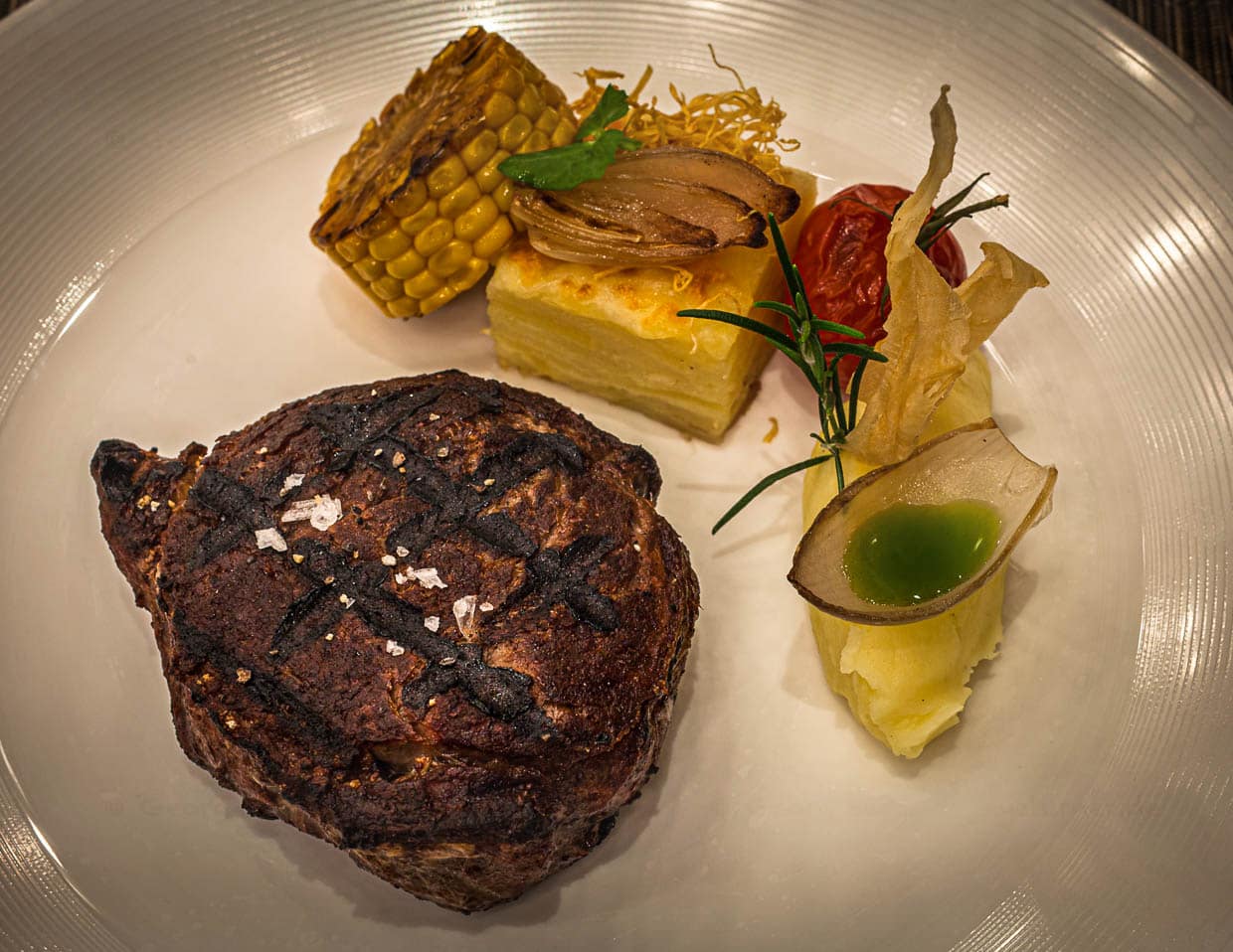 Ribeye vom Black Angus von hauseigener Weide, 28 Tage dry aged mit Kartoffelgratin und Püree mit Basilikumöl im Zwiebel-Schiffchen. Das Fleisch wird am Josper Grill zubereitet / © Foto: Georg Berg