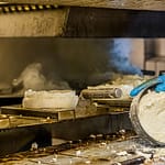 Die Käselaibe vom Morgen werden direkt aus der Ringform auf das Rondell der Räuchermaschine gelegt / © Foto: Georg Berg