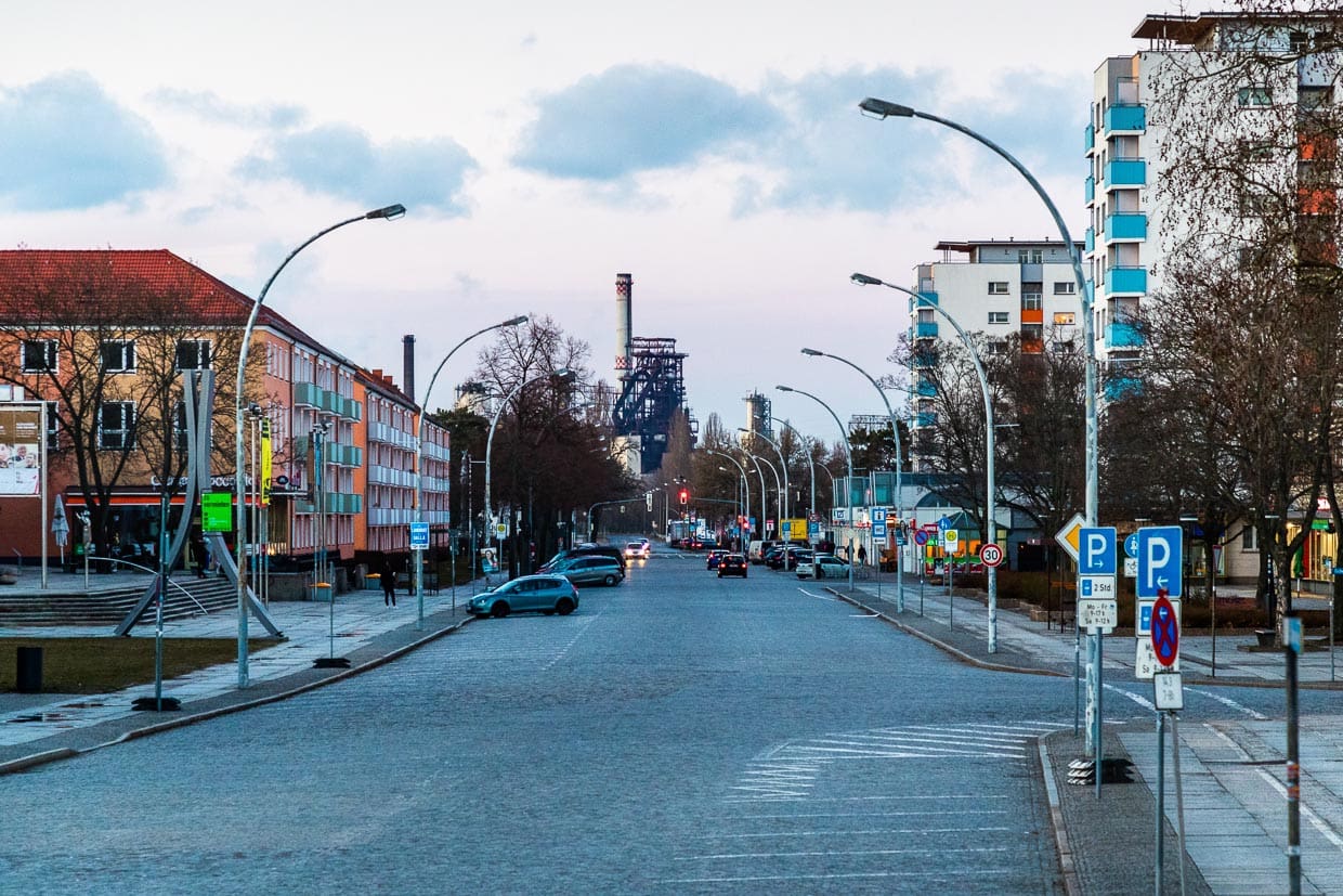Mittlerer Teil der Lindenallee (früher Leninallee) in Eisenhüttenstadt mit rhythmischer Abfolge von Hochhäusern mit auskragenden Dächern und Ladenlokalen. Am Ende der Allee Blick auf den großen Hochofen / © Foto: Georg Berg