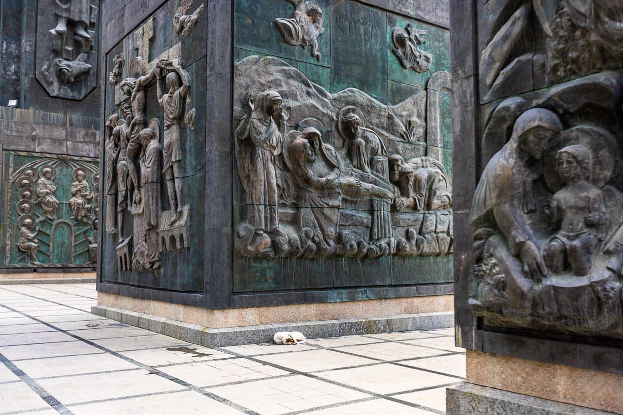 Ein Hund döst in der Chronik von Georgien, einer monumentalen Skulptur in den Nähe von Tbilisi, der Hauptstadt Georgiens. 16 Säulen erheben sich 35 Meter hoch. Im unteren Bereich sind biblische Szenen dargestellt. Darüber sind für die Geschichte Georgiens bedeutende Persönlichkeiten abgebildet. Begonnen wurde das Monument 1985 vom Bildhauer Surab Zereteli und ist bis heute noch nicht fertig gestellt / © Foto: Georg Berg