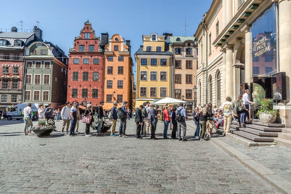 Stortorget, en la plaza central del casco antiguo de Estocolmo, la gente hace cola frente a la entrada del Museo del Premio Noble. Al fondo, los famosos y coloridos frontones de las casas / © Foto: Georg Berg