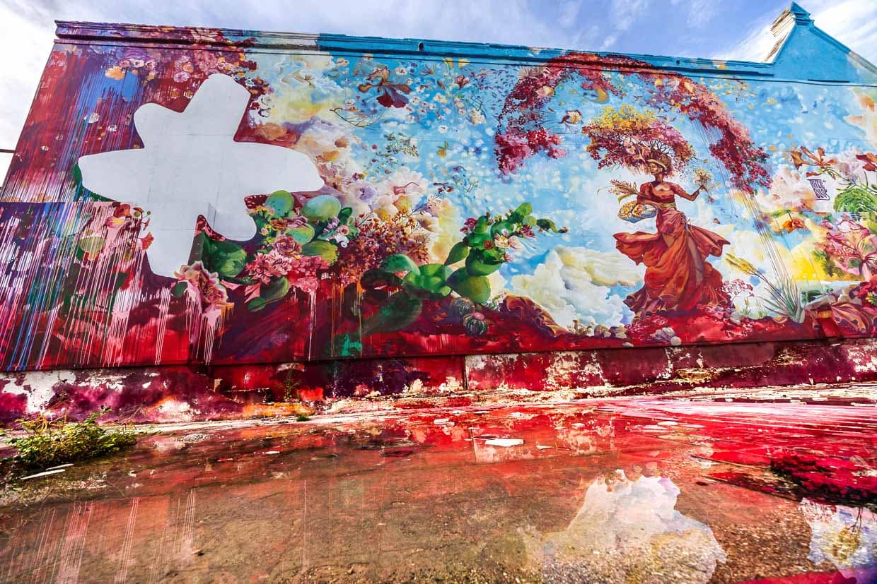 Enorme mural Djosa de Francis Sling en Willemstad. El artista escribe sobre la obra en otra pared junto al gran cuadro: Yo-Sa es mitad papiamento y mitad español. Djosa es la cuestión de qué es Dios. ¿Es un hombre o es una mujer? ¿Existe o es un mito? Es una larga discusión que a menudo termina con la pregunta: