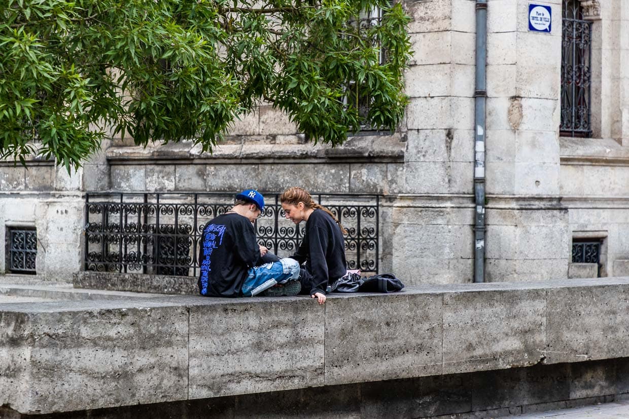 Alltag in Angoulême: Zwei junge Menschen sitzen auf der Mauer am Rathaus – erkennbar an der Sprechblasen-Beschriftung – und teilen einen Moment digitaler Zweisamkeit. Comics und Gegenwart verschmelzen / © Foto: Georg Berg