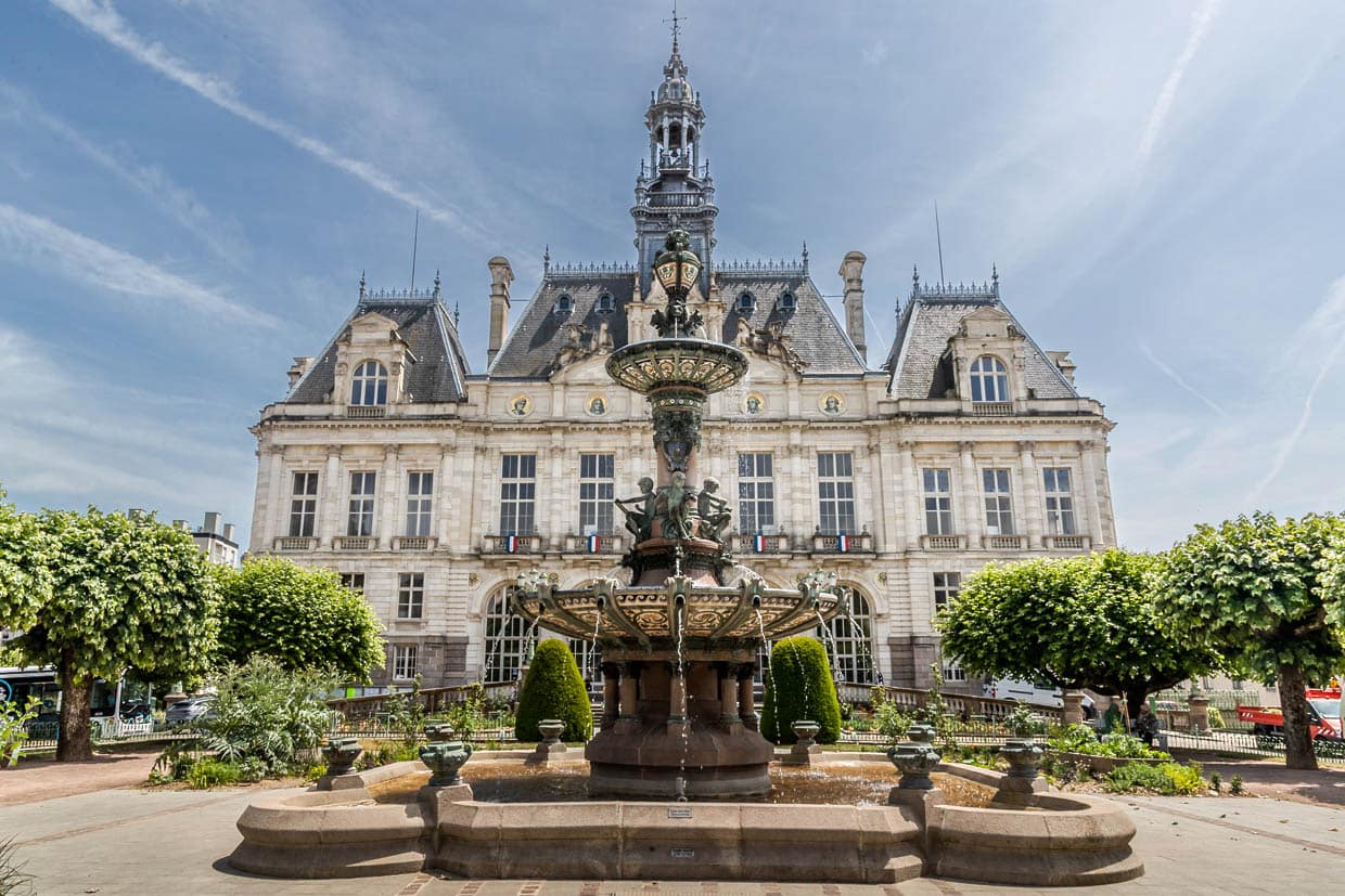 Ayuntamiento de Limoges con la fuente y la elegante fachada con un gran reloj y cuatro retratos de importantes personalidades inmortalizados en la fachada de piedra caliza. El ayuntamiento se levanta en el emplazamiento del antiguo foro de la ciudad y es una joya arquitectónica muy inspirada en la arquitectura de los ayuntamientos parisinos / © Foto: Georg Berg
