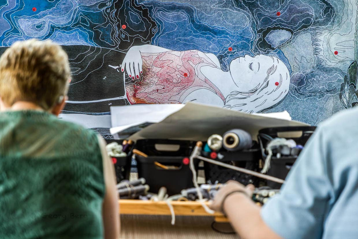 Cartonage mit einem Ausschnitt aus dem Motiv des Teppichs "Hommage à George Sand" von Francoise Petrovitch. Die Künstlerin legt besonderen Wert auf harmonische Übergänge, fragmentierte Farbfelder und subtile Düsterkeit. Die Tapisserie verbindet kräftige und zarte Farbbereiche, um poetische, aber dennoch gesellschaftskritische Bildwelten zu erzeugen. Die Webtechnik und Farbumsetzung erfolgen in enger Zusammenarbeit mit den lokalen Färberinnen und Weberinnen, um die gewünschte Nuancierung und Tiefenwirkung der Tuschezeichnungen der Künstlerin in textile Form zu übersetzen / © Foto: Georg Berg