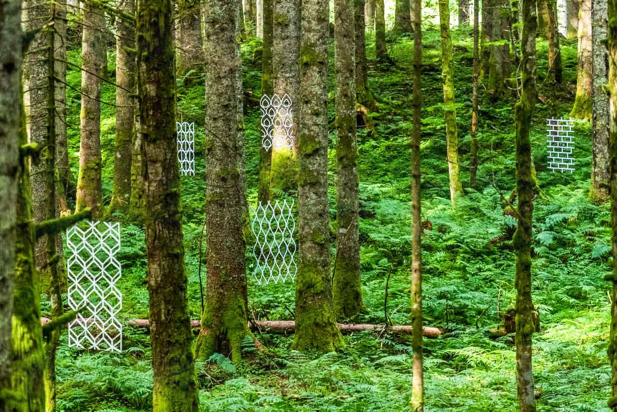 Naturkunstwerk „Durchblick“ von Susanne Ruoff aus Deutschland. Dünne Platten mit floralen und naturnahen Ornamenten freihängend zwischen Bäumen. Landart Pfad Gerschnialp in Engelberg 2025 / © Foto: Georg Berg