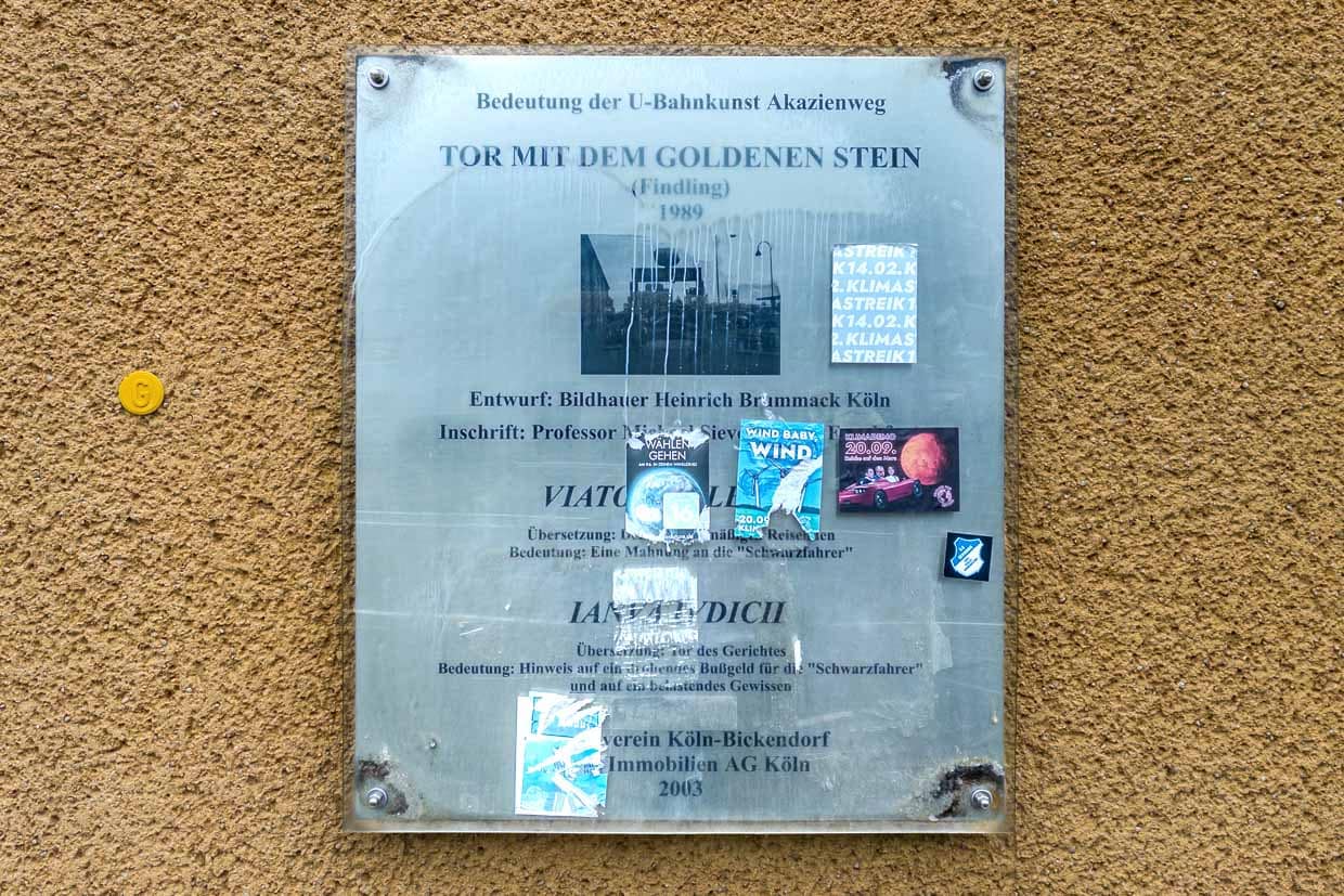 Informationstafel zum Kunstwerk Tor mit dem goldenen Stein hängt an einer Wand an der Venloer Straße, Cologne, Germany