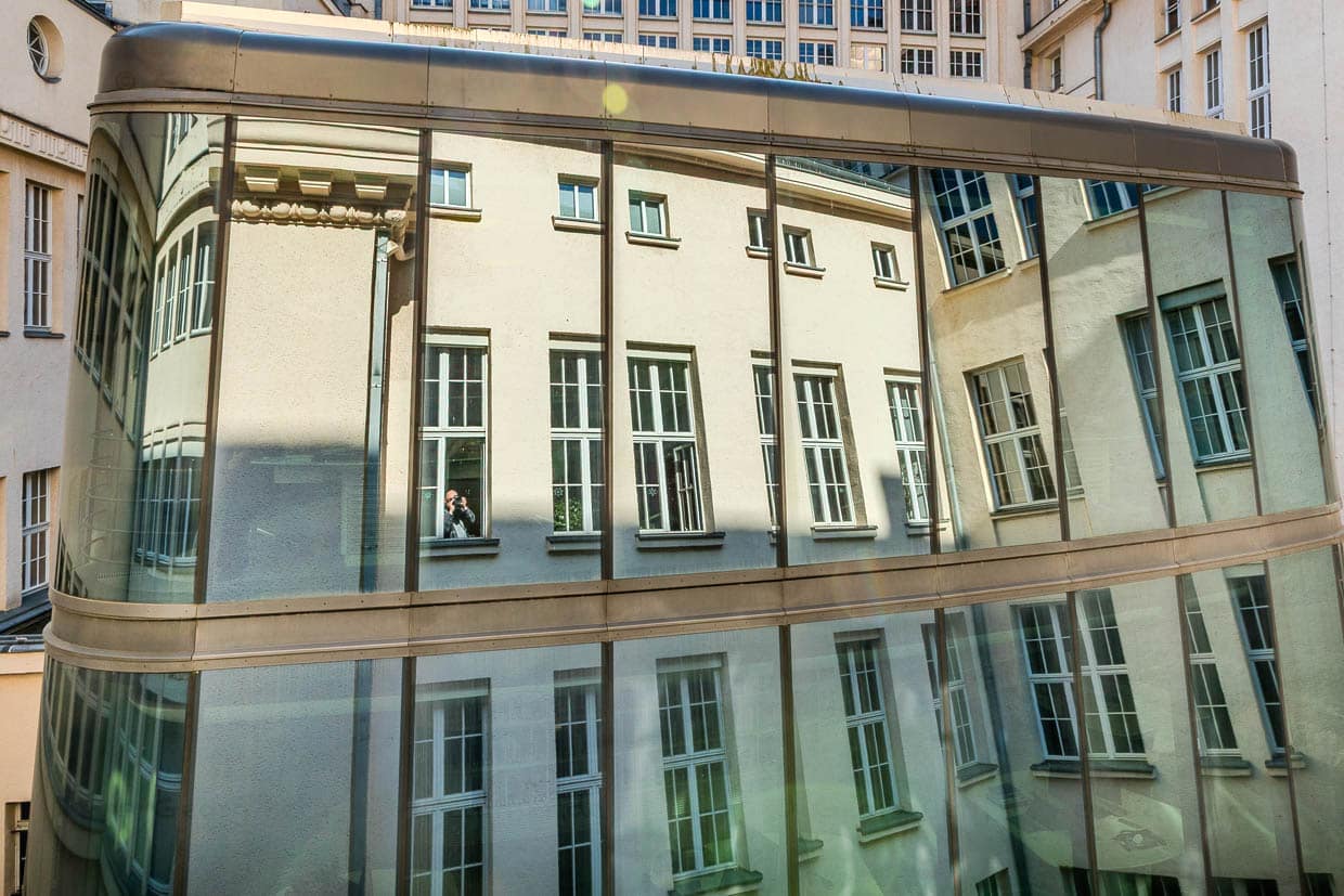 Mann mit Kamera fotografiert sich gespiegelt im Fenster eines modernen Gebäudes in Leipzig, Deutschland