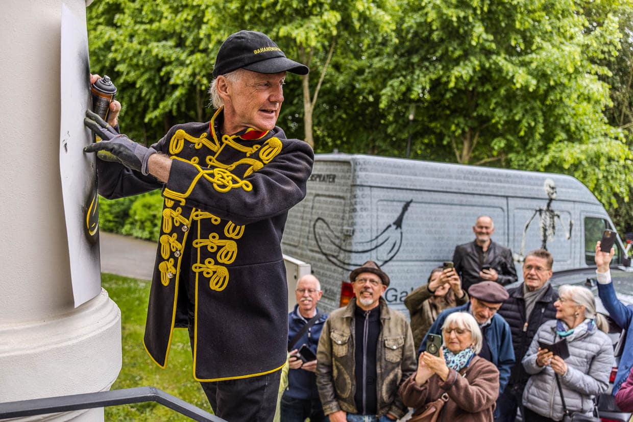 Ein als Offizier gekleideter Künstler sprüht ein Bananen-Motiv auf eine Säule am Stadtpark, Grevenbroich, Deutschland