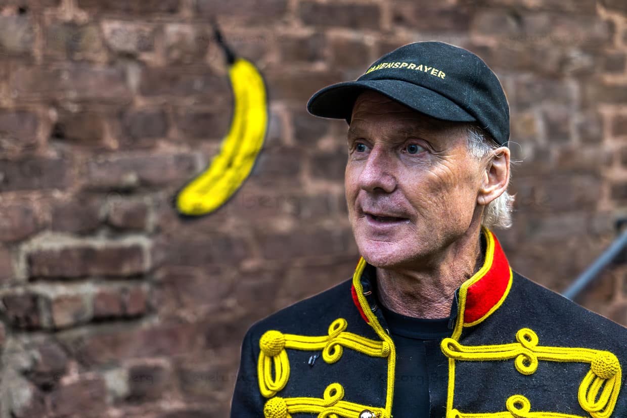 Ein Mann in Uniformjacke und Kappe steht vor einem Bananen-Graffiti am Stadtpark, Grevenbroich, Deutschland