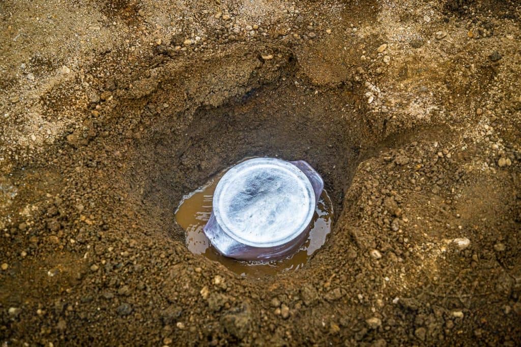 Brottopf mit Deckel und in Folie gewickelt und in einem Erdloch an den heißen Quellen von Laugarvatn. Der Topf steht in kochend heißem Wasser. Er wird mit Erde bedeckt und nach 24 Stunden wieder herausgeholt. Solange benötigt das Roggenbrot, Hverabrauð, zum Garen / © Foto: Georg Berg