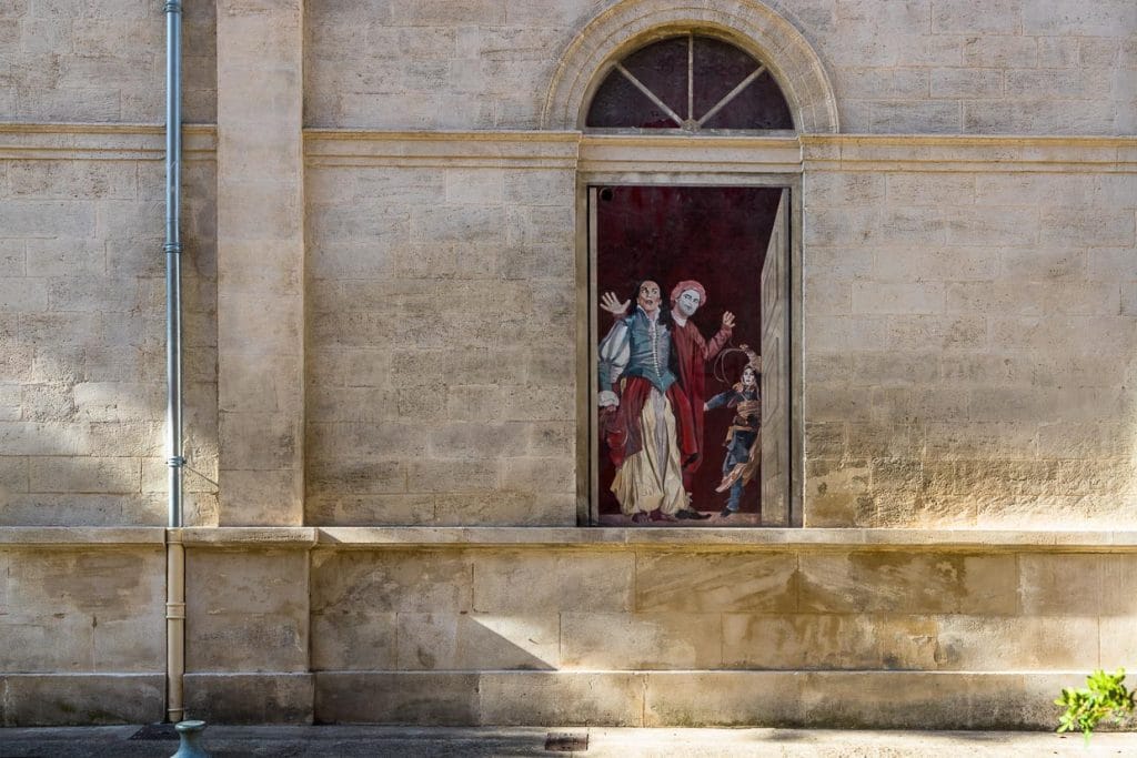Wandgemälde - Serie von Marion Pochy und Dominique Durand für das Theaterfestival von Avignon mit Bezug auf berühmte Inszenierungen. Hier die Nacht des Königs von William Shakespeare inszeniert von Ariane Mnouchkine, 1982, Rue Molière. 1986 begannen die Künstlerin Marion Pochy und der Künstler Dominique Durand mit der Gestaltung von zugemauerten Fenstern, die sich an vielen Gebäuden der Altstadt von Avignon finden.  / © Foto: Georg Berg