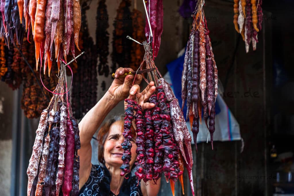 A saleswoman cuts sticks from Churchkhela. Churchkhela (ჩურჩხელა) is a Georgian confectionery. Nuts coated with pelamushi, a couverture made from boiled grape juice with starch flour without sugar / © Photo: Georg Berg