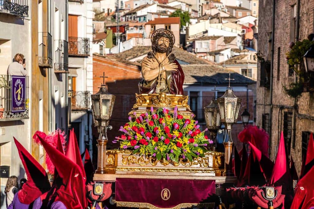 Procession in Spain with Jesus figure on a float and participants in red hoods. / © Photo: Georg Berg