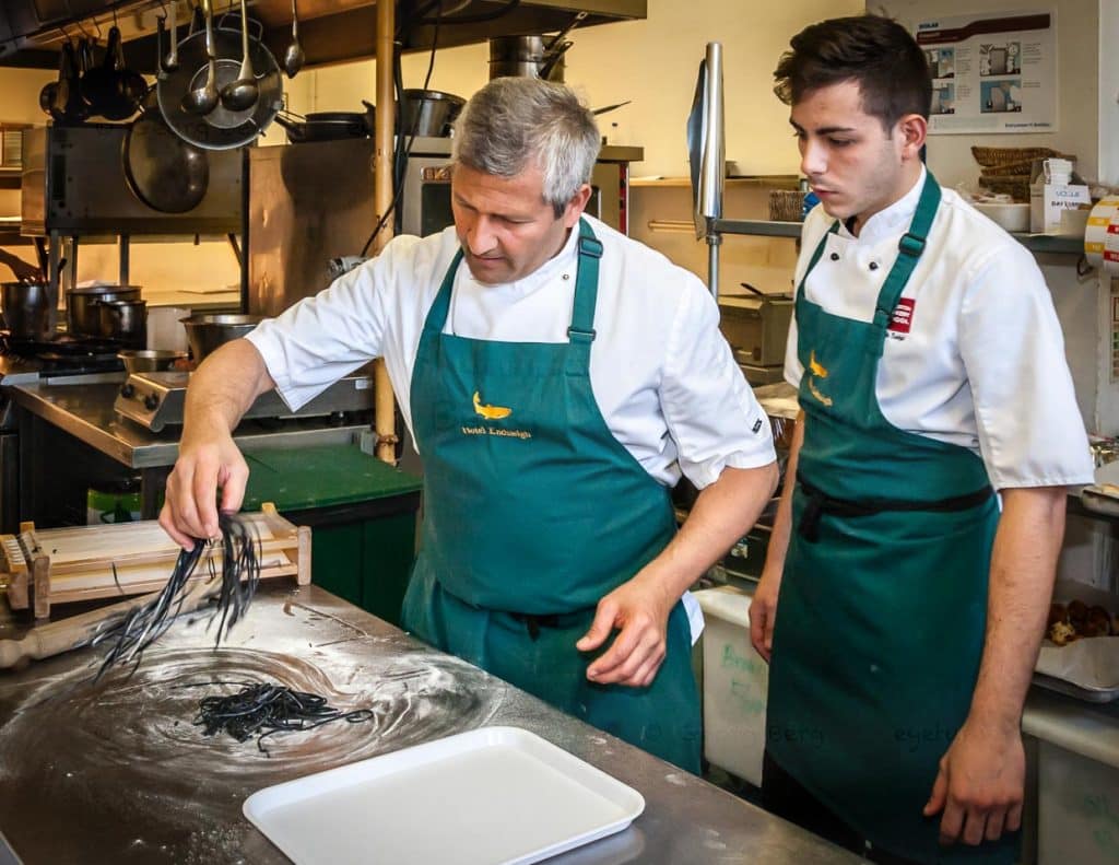 Die einzelnen Schritte der Pastaproduktion mit dem Carraturo. Zuerst wird der Teig mehrmals durch eine Nudelmaschine gedreht, bis er ganz dünn ist. Danach kann der dünne Teiglappen mit einem Nudelholz durch die Drähte gedrückt werden, die ihn in dünne Streifen schneiden. Anschließend kurz bemehlen und erst kurz vor dem Verzehr in Salzwasser al dente kochen. An der Seite des Chefkochs steht Salvatore Piacente, ebenfalls Absolvent der Kochschule Santa Maria, an der schon José Graziosi sein Handwerk lernte / © Foto: Georg Berg