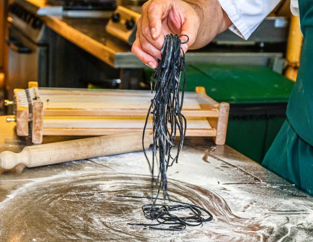 Die einzelnen Schritte der Pastaproduktion mit dem Carraturo. Zuerst wird der Teig mehrmals durch eine Nudelmaschine gedreht, bis er ganz dünn ist. Danach kann der dünne Teiglappen mit einem Nudelholz durch die Drähte gedrückt werden, die ihn in dünne Streifen schneiden. Anschließend kurz bemehlen und erst kurz vor dem Verzehr in Salzwasser al dente kochen. An der Seite des Chefkochs steht Salvatore Piacente, ebenfalls Absolvent der Kochschule Santa Maria, an der schon José Graziosi sein Handwerk lernte / © Foto: Georg Berg