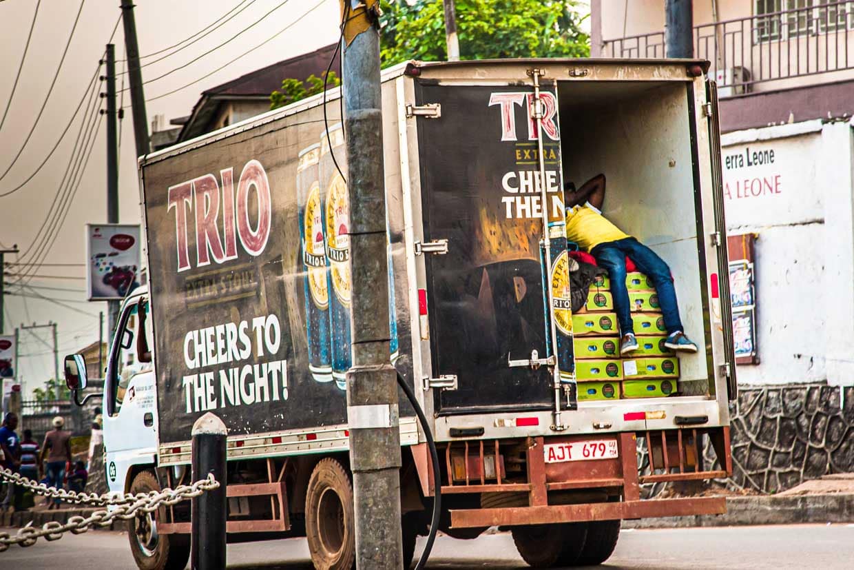 Ein Mann schläft auf der Ladefläche eines offenen Lastwagens der durch Freetown (Sierra Leone) fährt / © Foto: Georg Berg