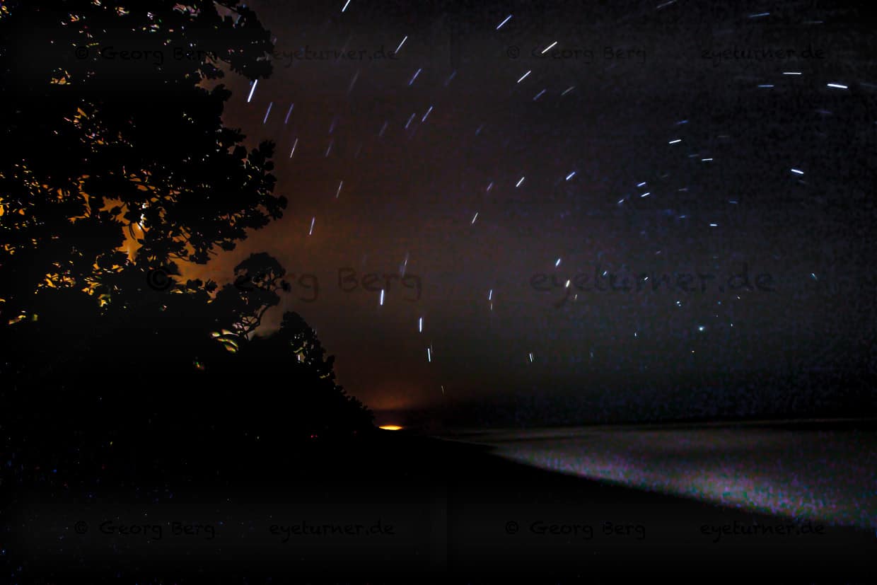 Wenn die Augen sich an die Dunkelheit gewöhnt haben, kann man außer den Sternen auch die Vegetation vor dem sogar hier gegenwärtigen Licht aus Siedlungen sehen. Auf der anderen Seite die von den Sternen beleuchtete Brandung / © Foto: Georg Berg