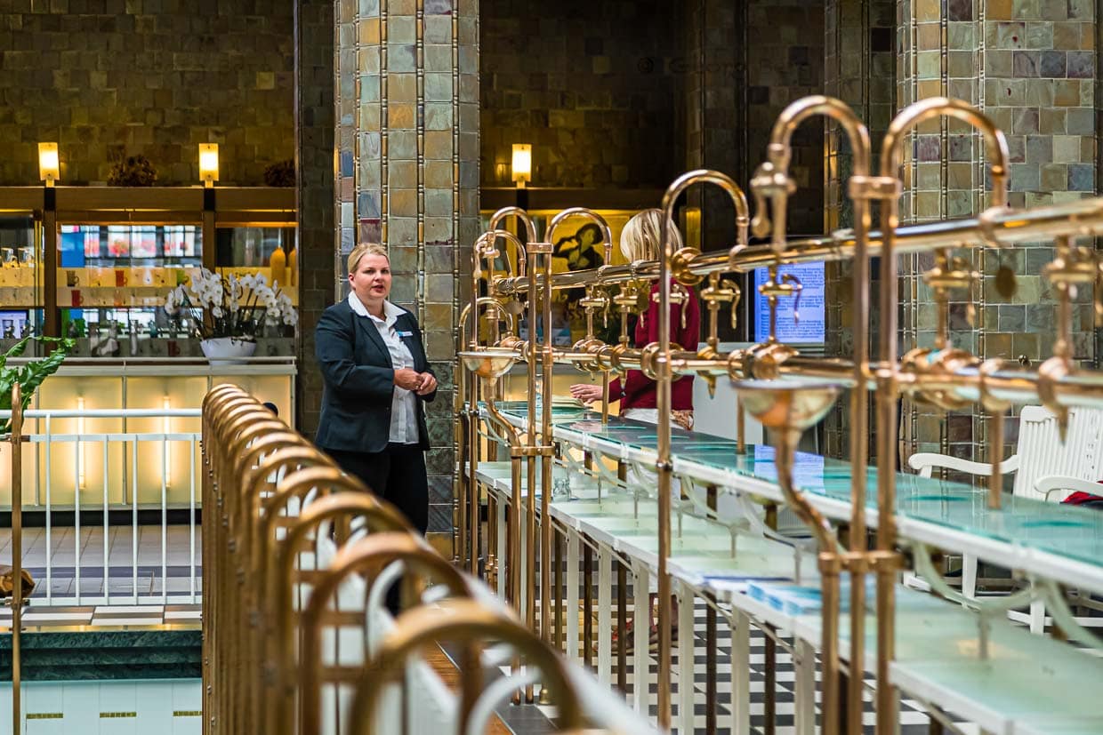 Blinkendes Messing. Eine Brunnenfrau inmitten der aufwändigen Zapfanlage. Der Kurgast kann aus den vier Heilwässern Pandur, Rakoczy, Max und Luitpold und dem Kissinger Bitterwasser wählen. Auf Wunsch nehmen die Brunnenfrauen die Kohlensäure aus dem Wasser / © Foto: Georg Berg