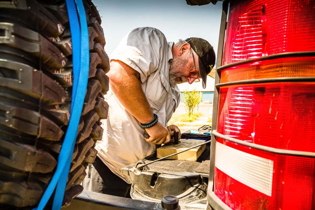 Unterwegs wird der Kofferraum des Landrovers zur Werkbank. Konrad Fobbe fertigt aus einem Stück Gummischlauch ein Ersatzteil / © Foto: Georg Berg