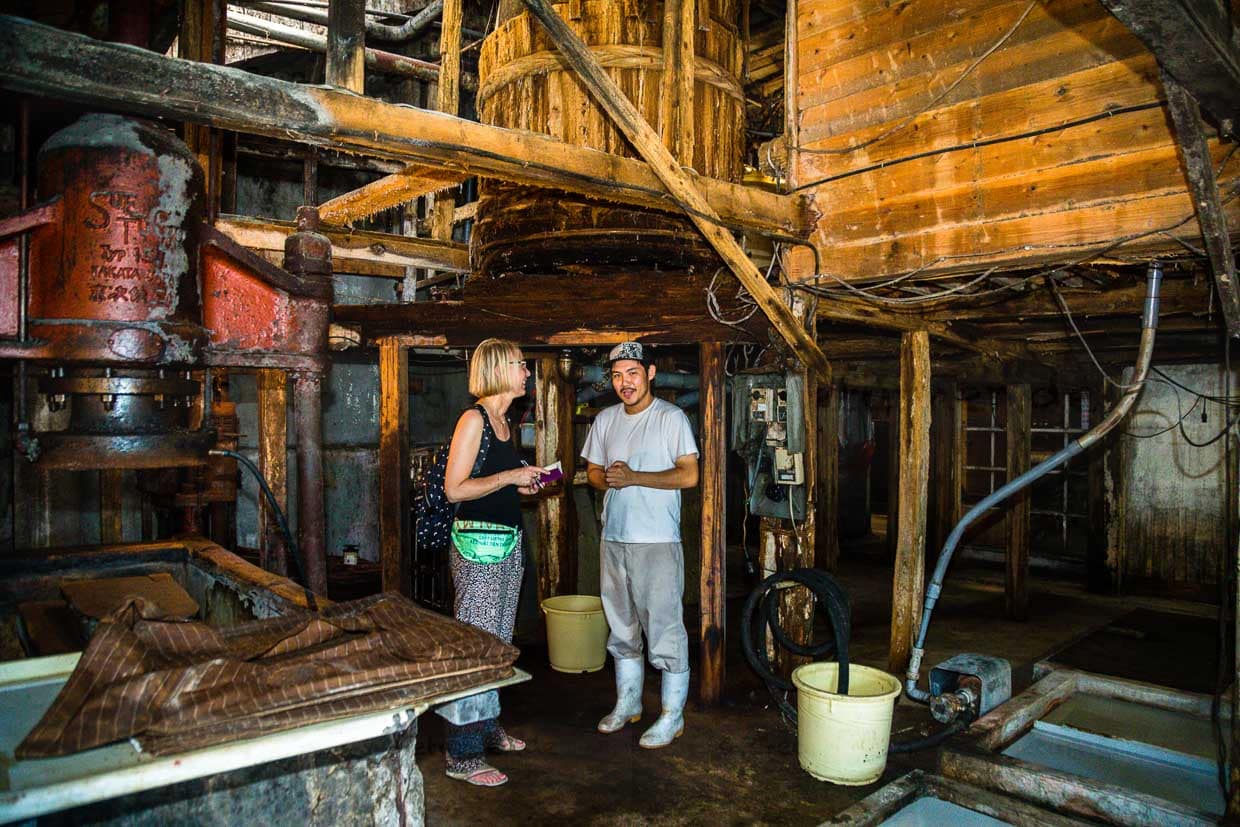 Shohei Nozue erklärt Reporterin Angela Berg, dass das Moromi im Sommer alle sieben Tage und im Winter alle 14 Tage mit einem großen Paddel gerührt wird. Fermentation und Zeit sind die wichtigsten Komponenten für eine hochwertige Sojasauce / © Foto: Georg Berg